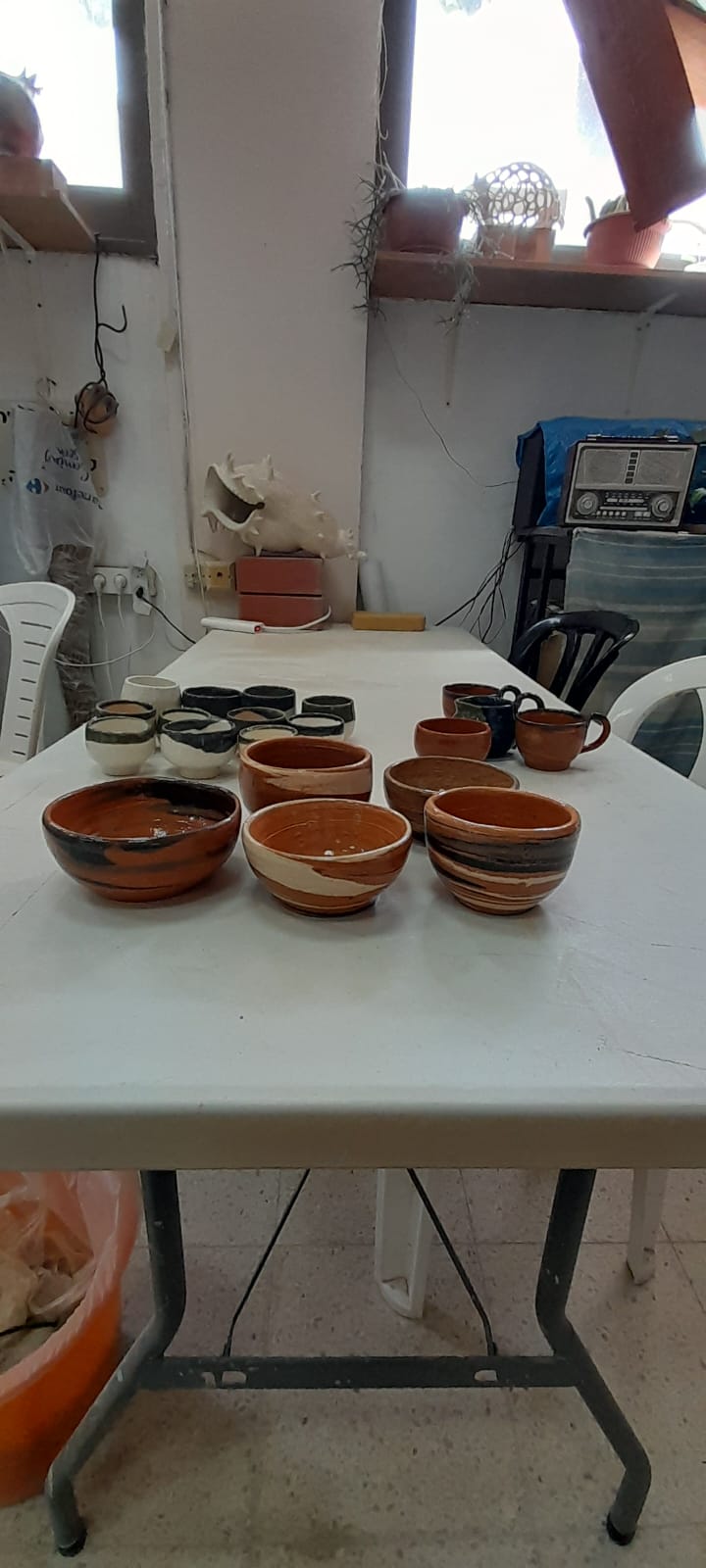 שולחן לבן ועליו מגוון קערות וכוסות קרמיקה בגווני חום ושחור