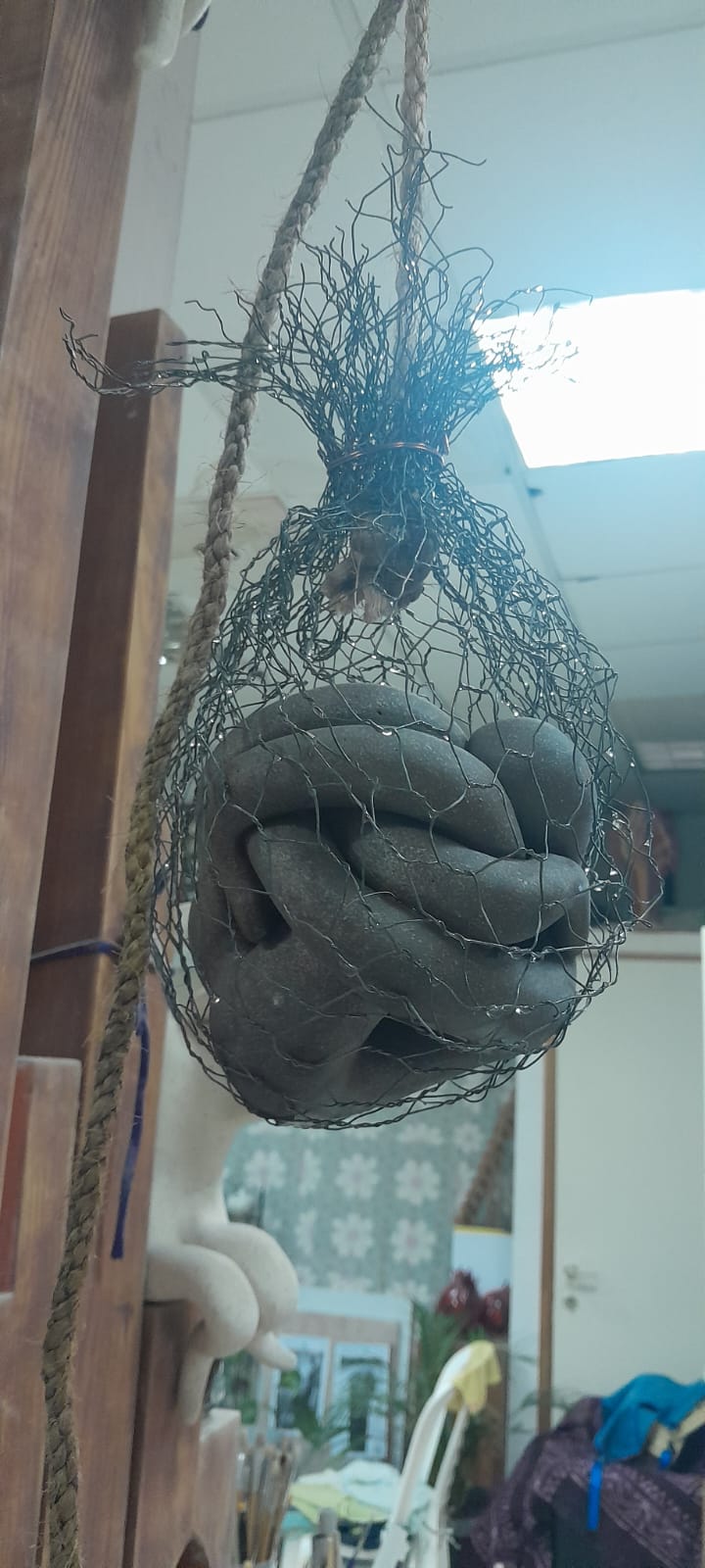 פסל אבסטרקטי מחימר אפור תלוי ברשת מתכת