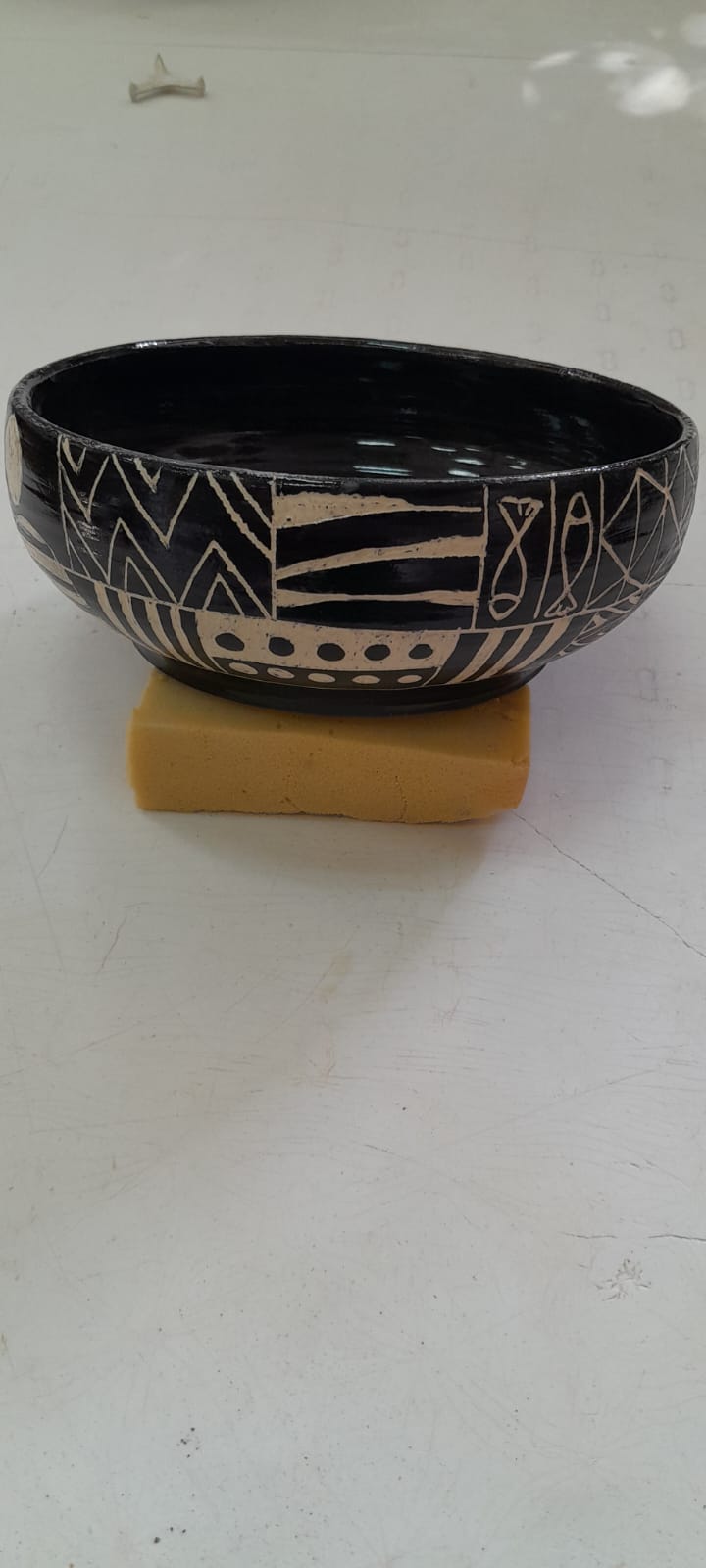 קערת קרמיקה שחורה עם עיטורים גיאומטריים לבנים, מונחת על ספוג